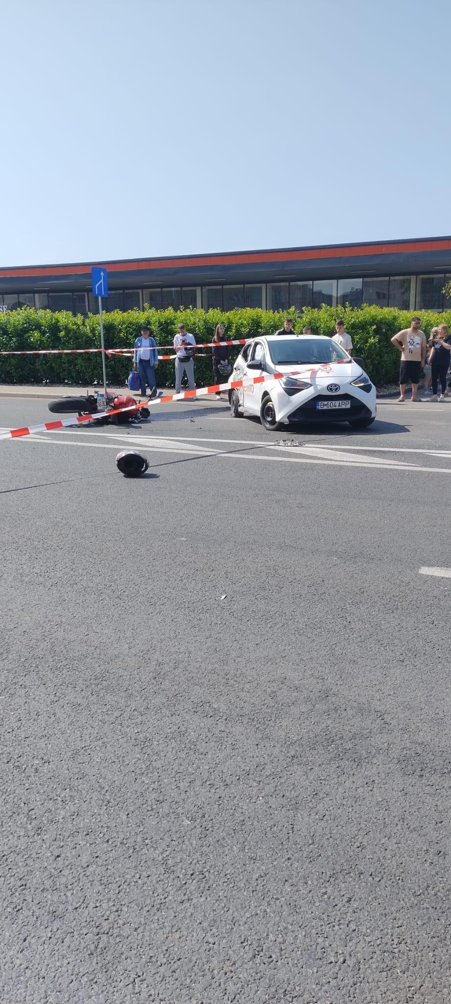 un autoturism lovit, o motocicletă zdrobită și o cască de motociclist pe asfalt